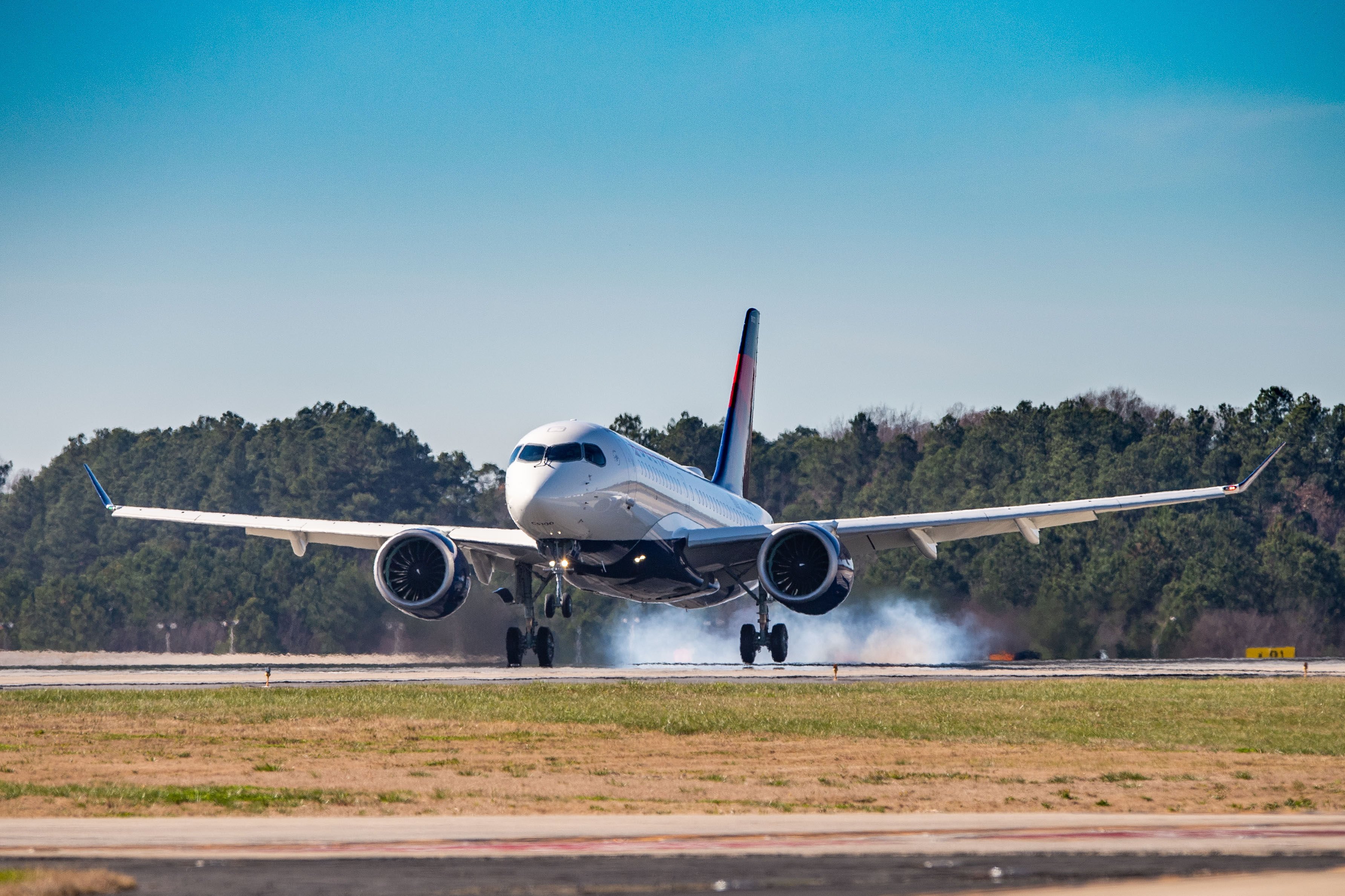 A Delta Air Lines A220 landing on a runway.