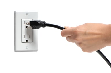 Hand removing a plug from a wall outlet