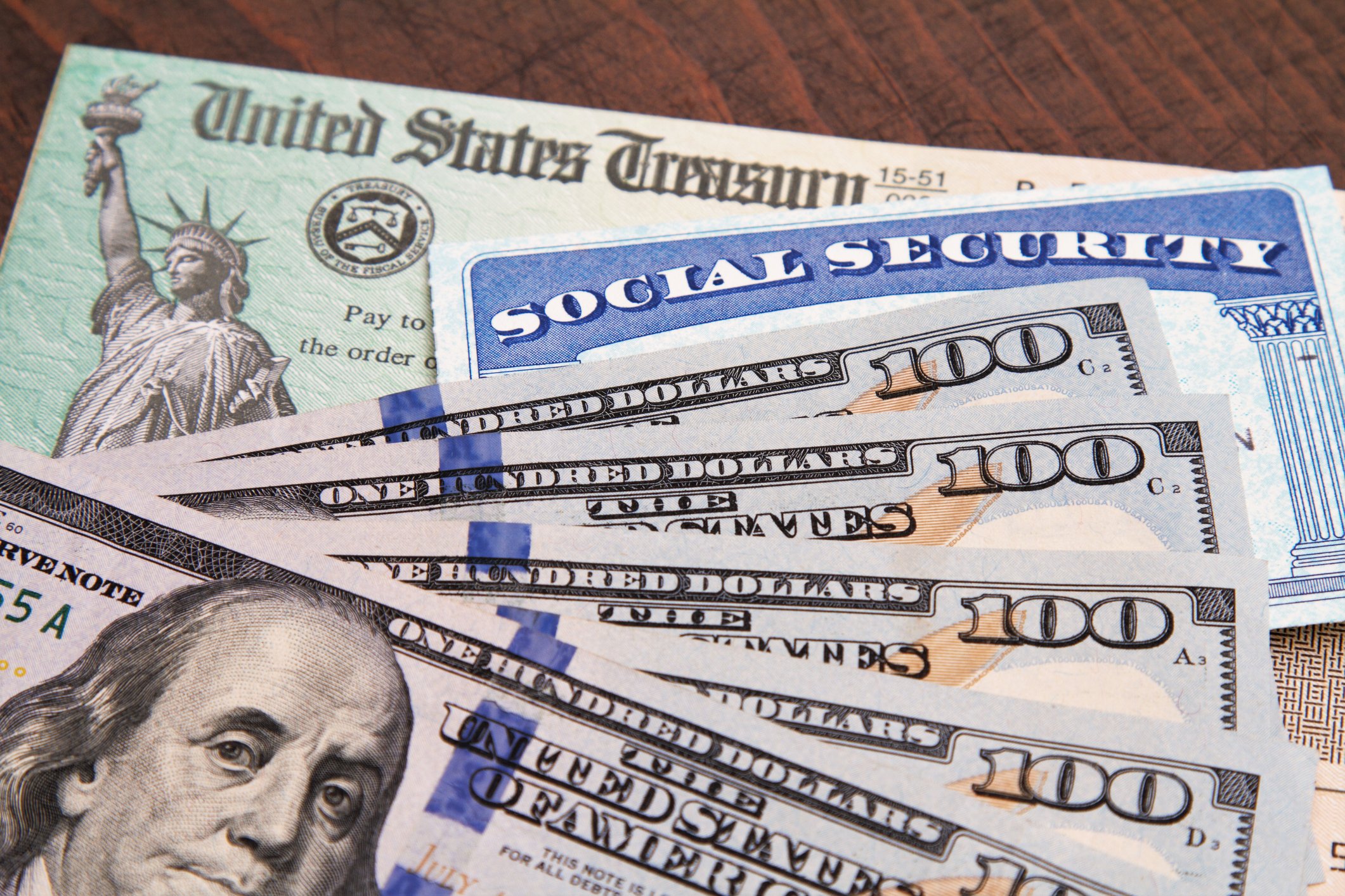 Five $100 bills fanned out atop a Social Security card and a U.S. Treasury check.