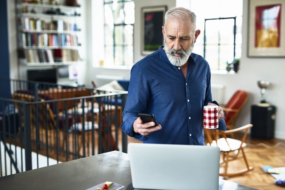 A person checking their phone in front of a laptop.