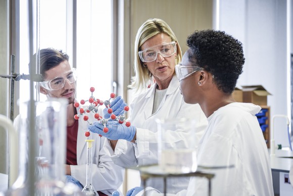 Three scientists wearing lab coats, working with a molecular model in a life sciences lab.
