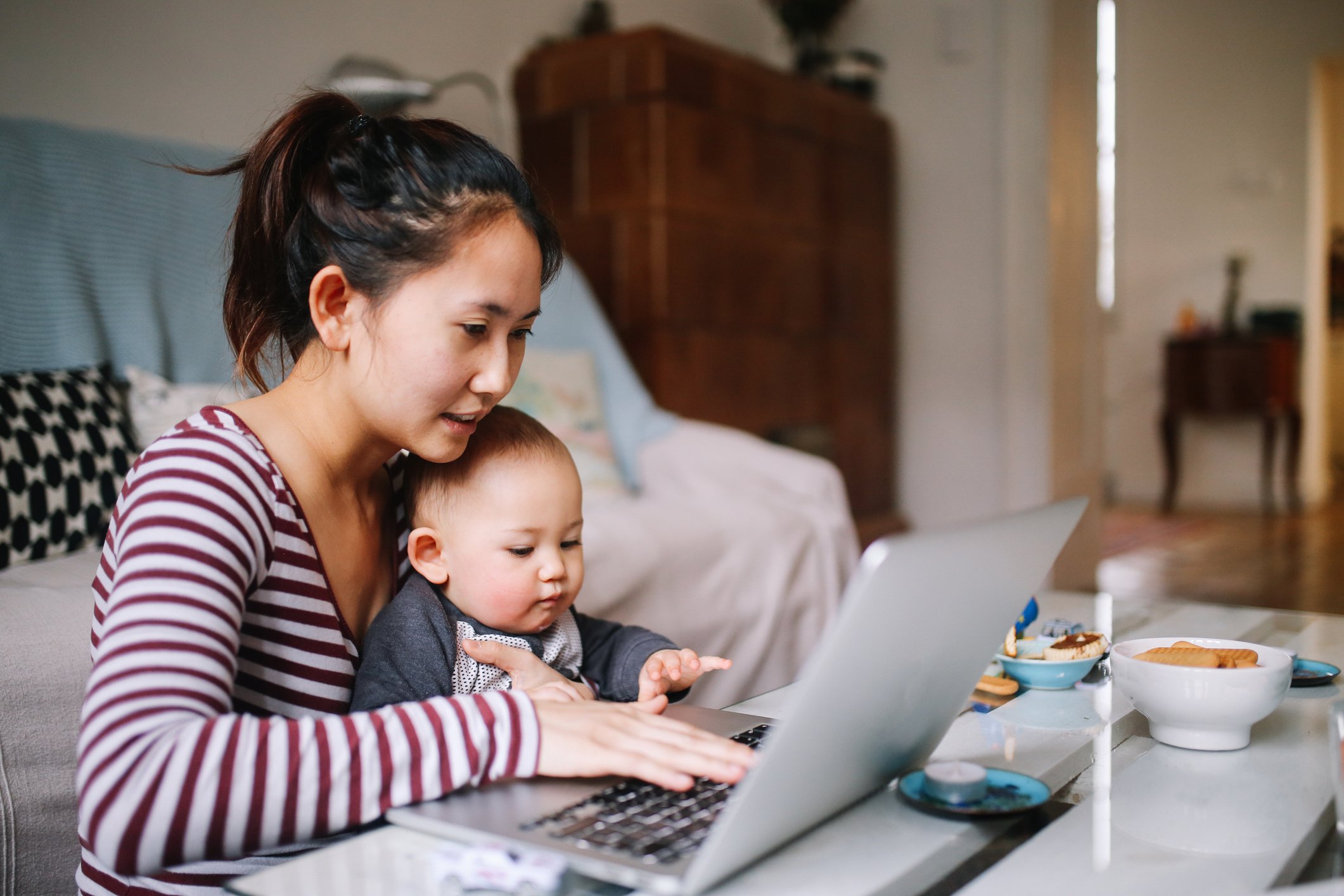 A person at a laptop holding a baby.