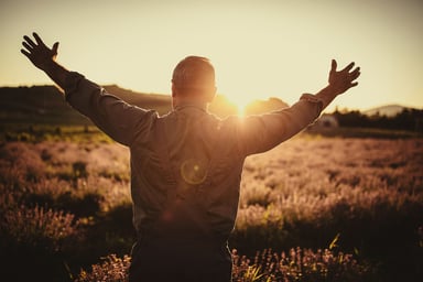 person puts arms out as sun rises