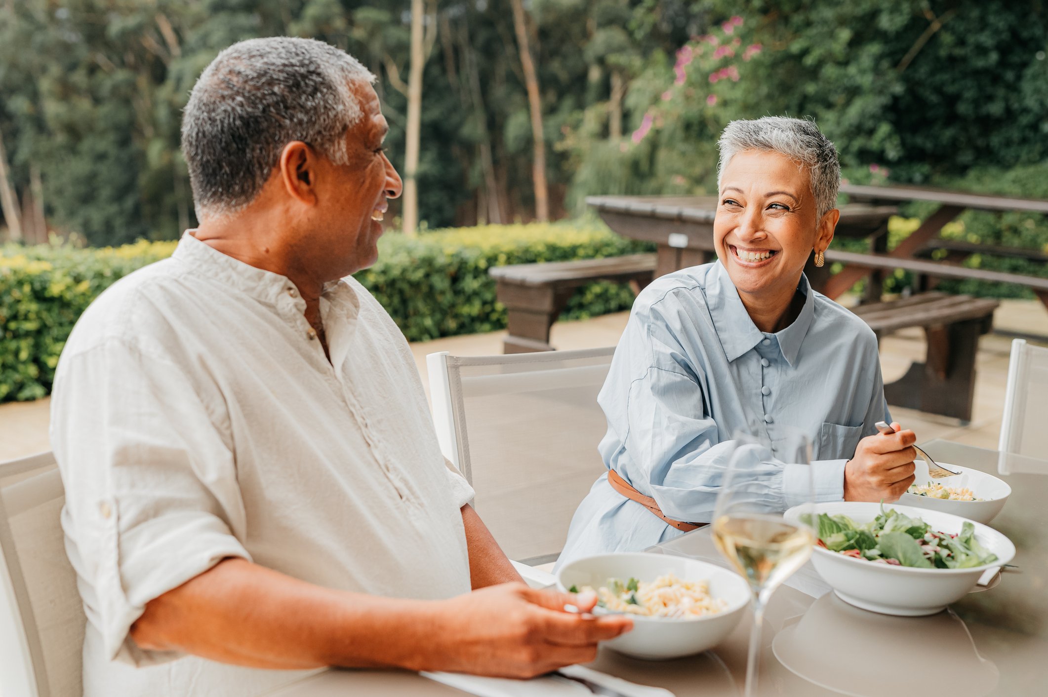 Two people sitting at a table eating salad and drinking wine.