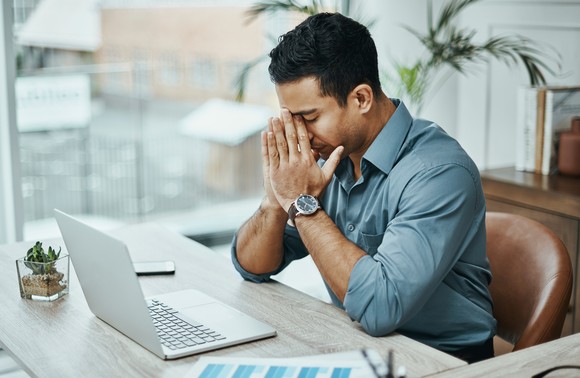 A person holding hands to face while sitting in front of a laptop.