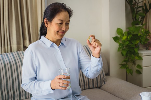 A smiling person holding a pill and a glass of water.