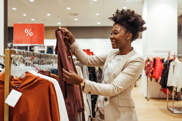 Person in a clothing retail store pulling a shirt from a rack.