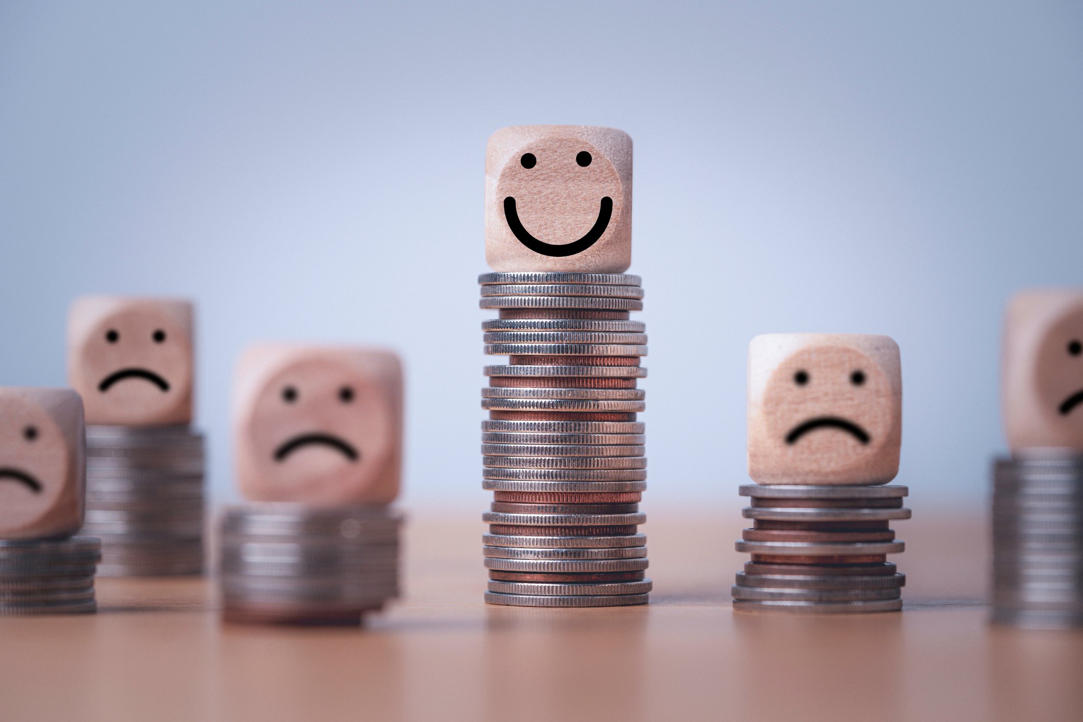 One happy face on top of a stack of coins, surrounded by sad faces on top of smaller stacks.