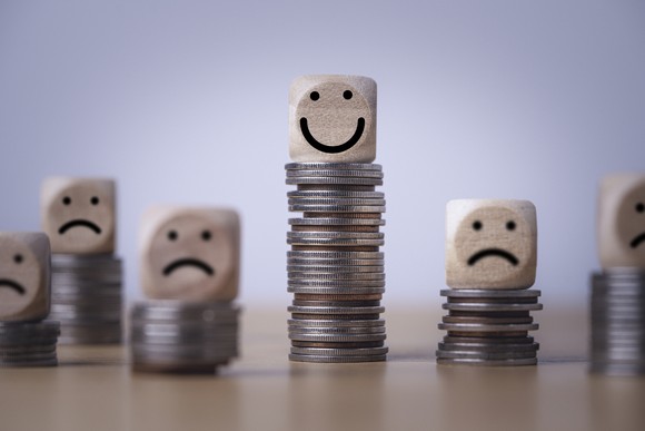 One happy face on top of a stack of coins, surrounded by sad faces on top of smaller stacks.