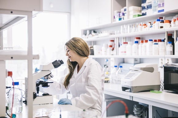 A scientist sits in a laboratory observing her samples underneath a microscope.