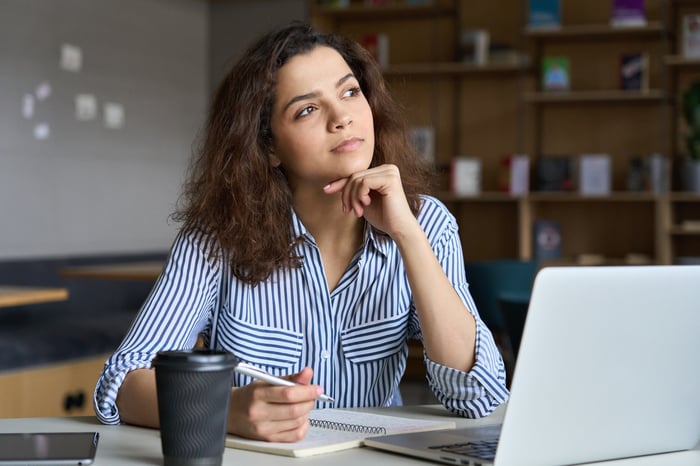 A person looking off, thinking, while sitting at a desk. 
