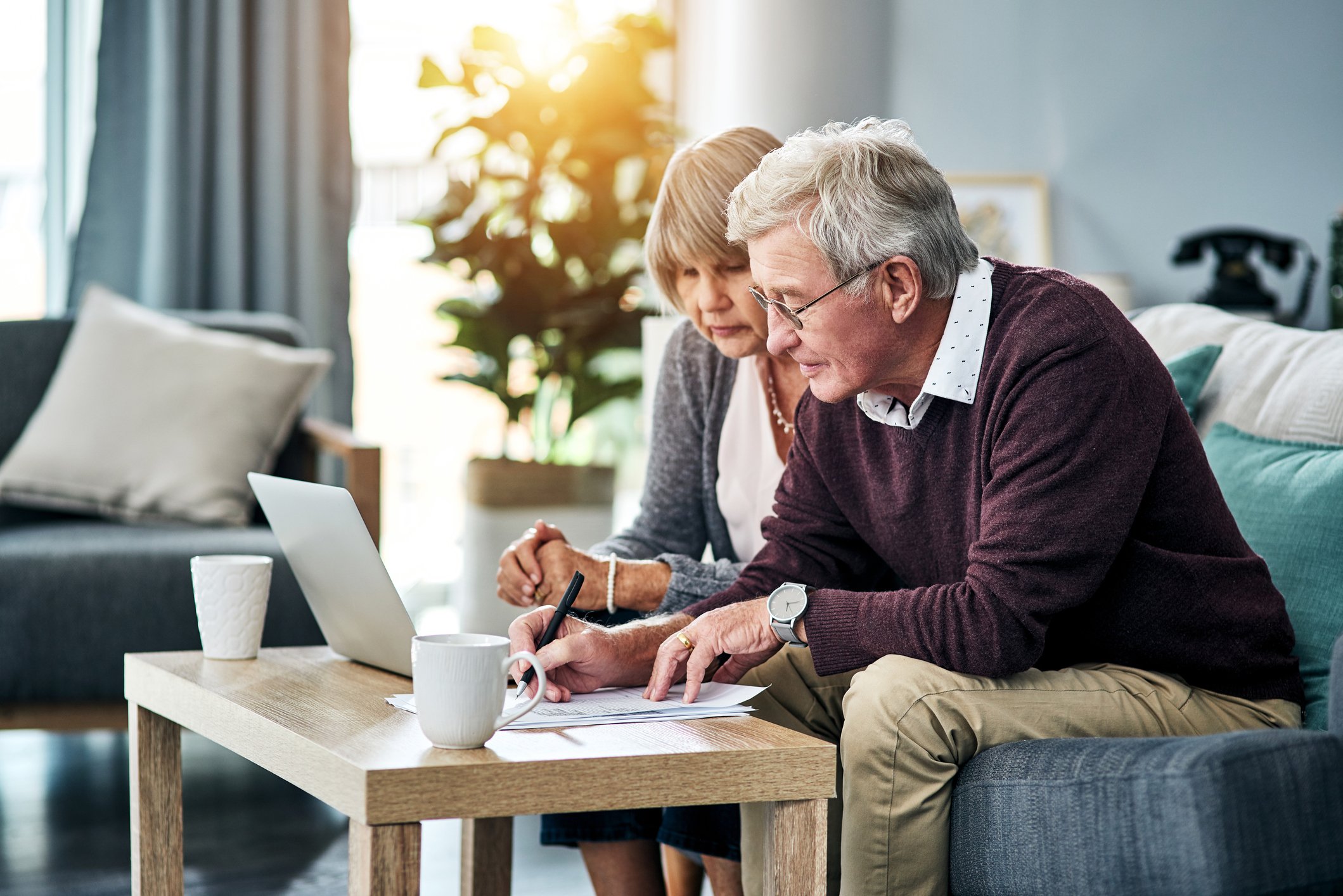 A retired couple sits on couch while looking at a laptop screen.