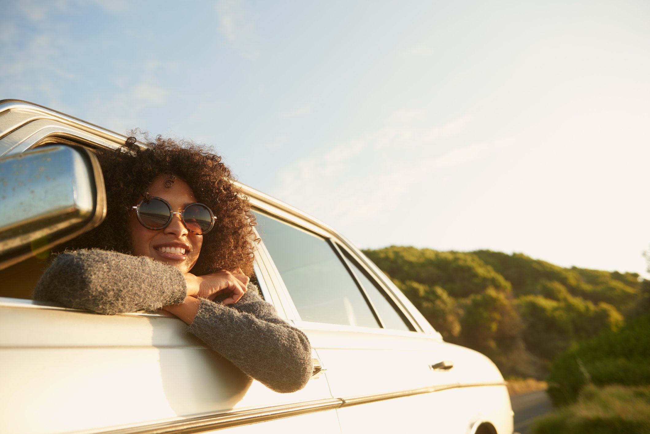 A person wearing sunglasses smiles while leaning out of a car. 