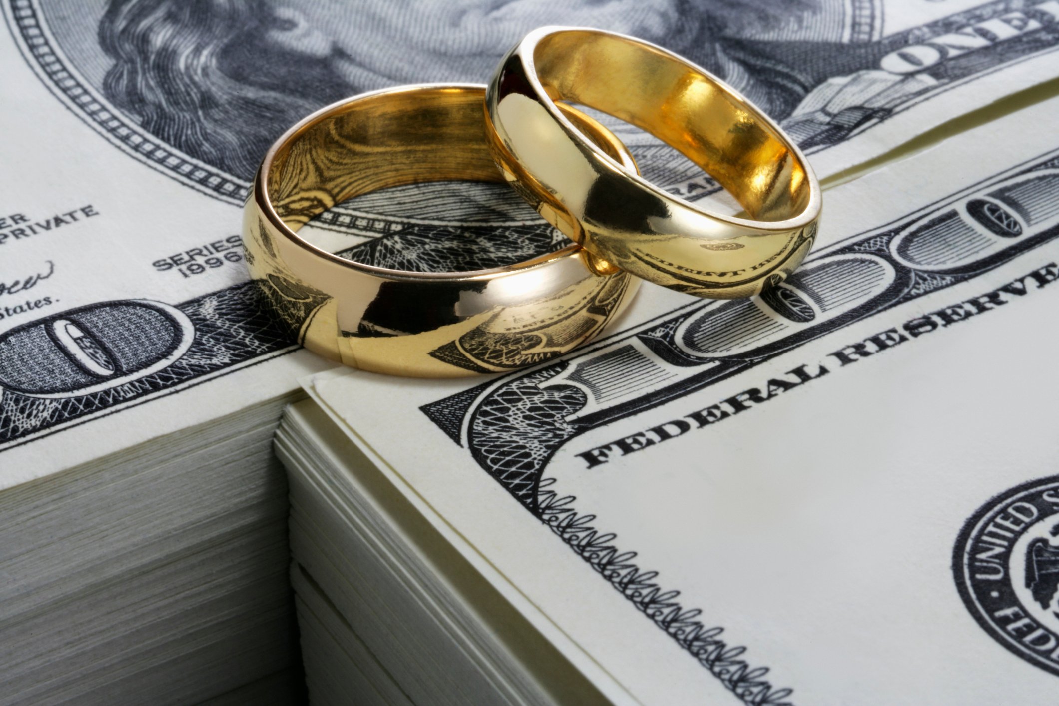 Two wedding rings sitting on stacks of one hundred dollar bills.
