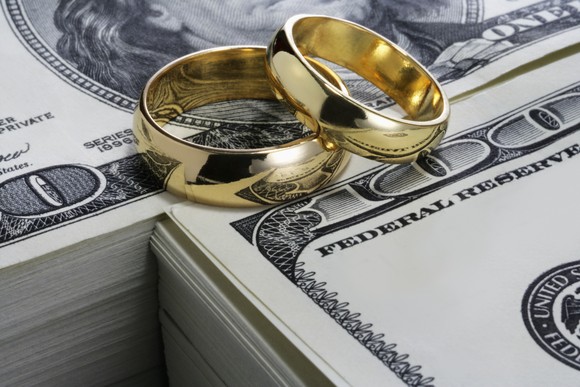Two wedding rings sitting on stacks of one hundred dollar bills.