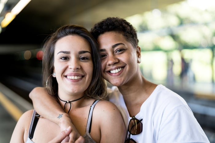 A couple is smiling at the camera, one with her arm around the other.