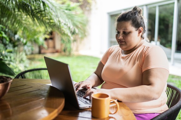Someone sitting at a table typing on a laptop with a coffee mug beside them.