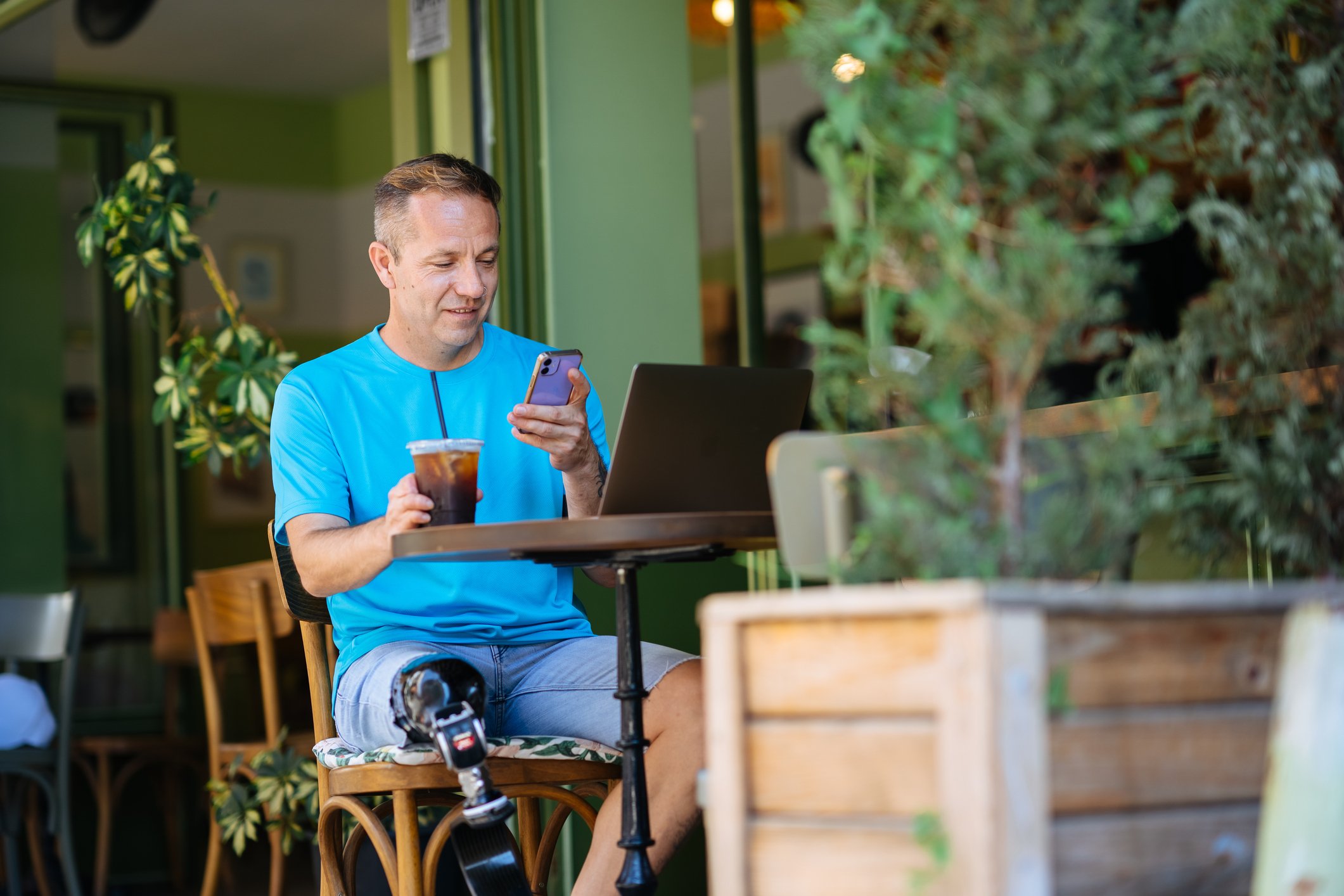 Someone sitting at a table holding an iced coffee and their phone.