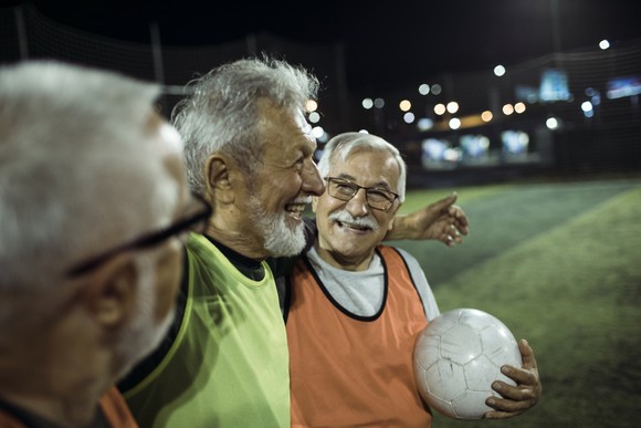 Three people on a soccer field smiling while one is holding a soccer ball.