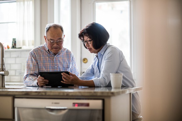 Two people sitting in a kitchen looking at a tablet.