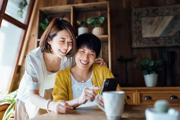 Two people at a table smiling as they look at something on one of their smartphones.