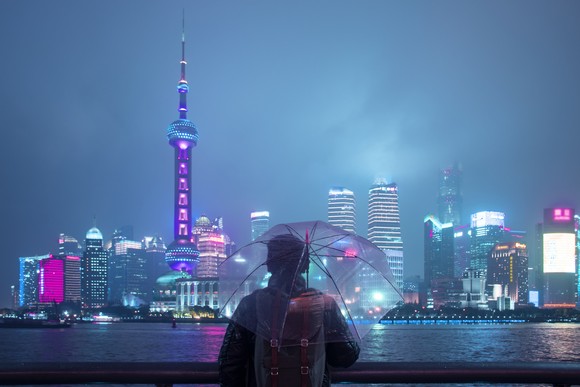 A person holds an umbrella in Shanghai while looking at the skyline at night. 