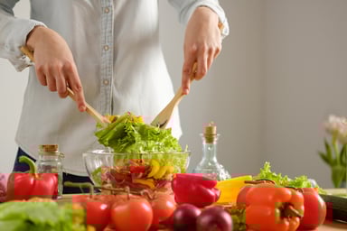 Chef tossing a salad in a glass bowl.
