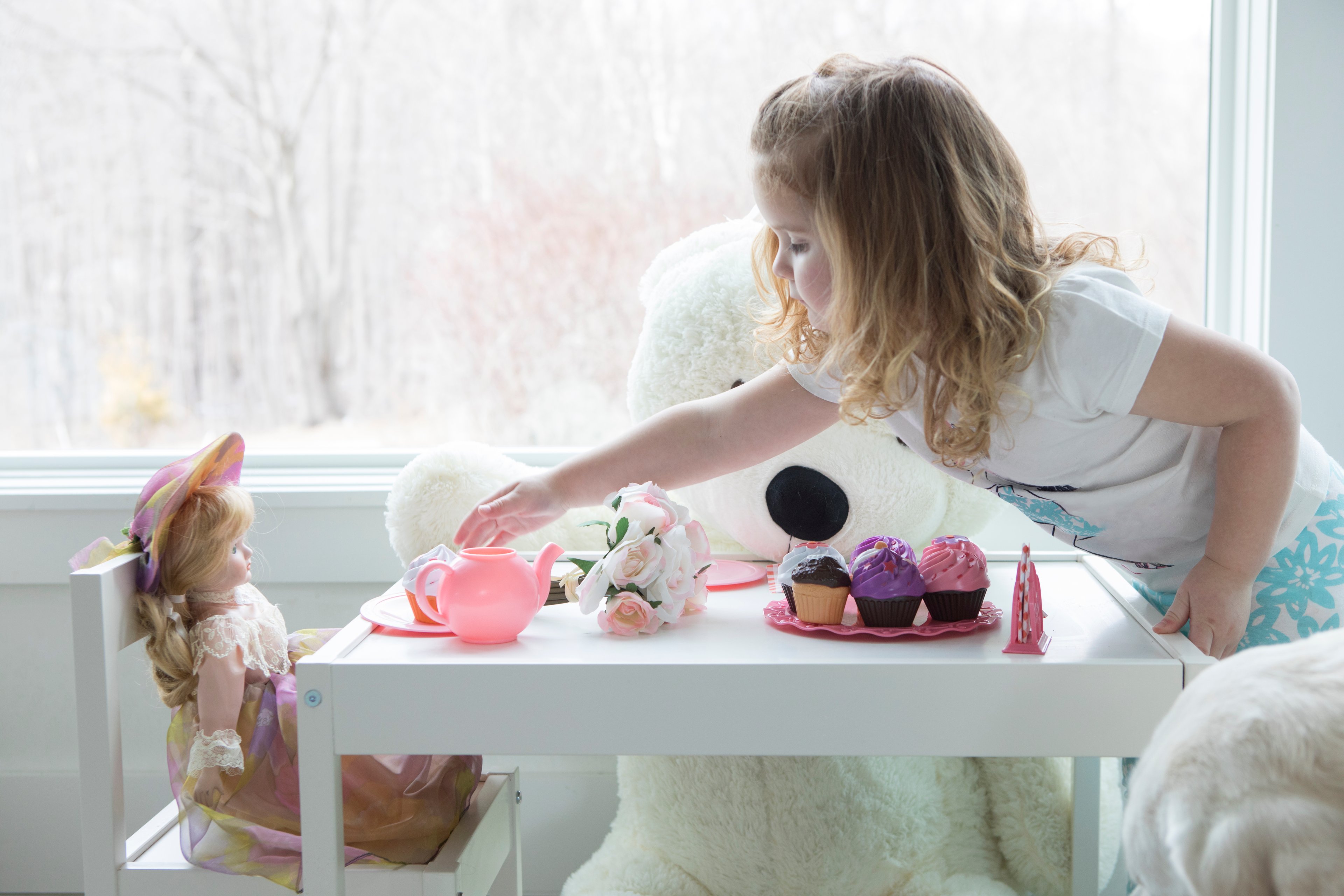 A child sitting in their bedroom playing with dolls and toys.