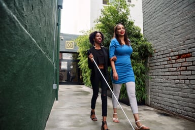 Two people walking one with a seeing stick