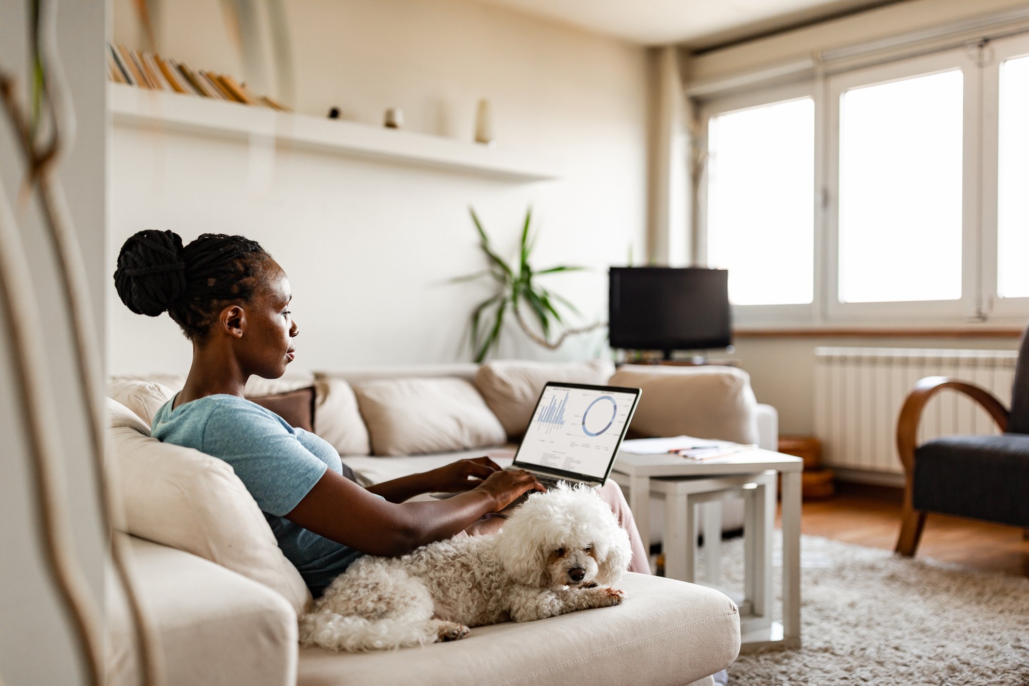 Someone sitting on a couch using a laptop with a dog beside them.