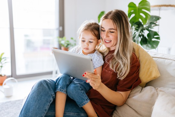 A child sitting on someone's lap while they look at a tablet.