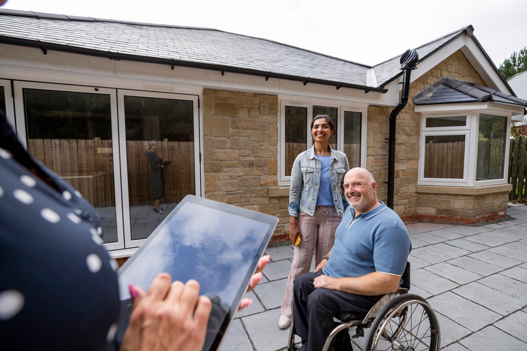 Two people, one in a wheelchair, on patio of a new home. 