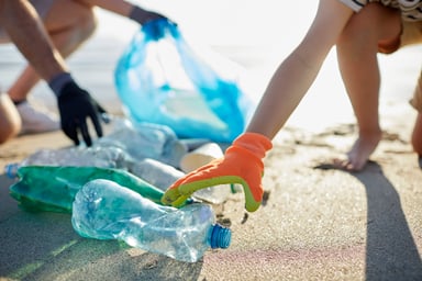 Two persons collecting plastic bottles on a beach.