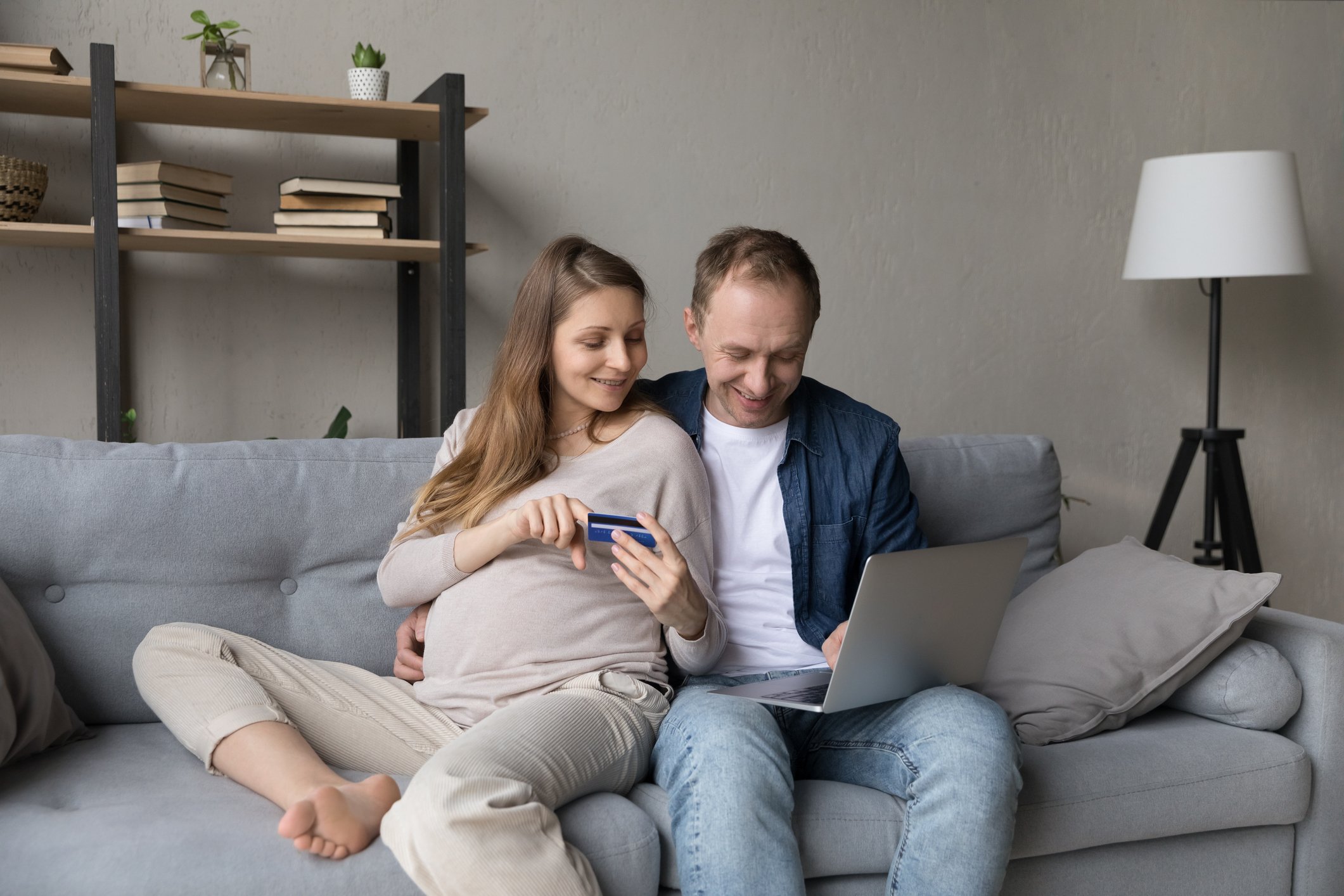 Two people sitting on a couch using a laptop with one person holding a credit card.