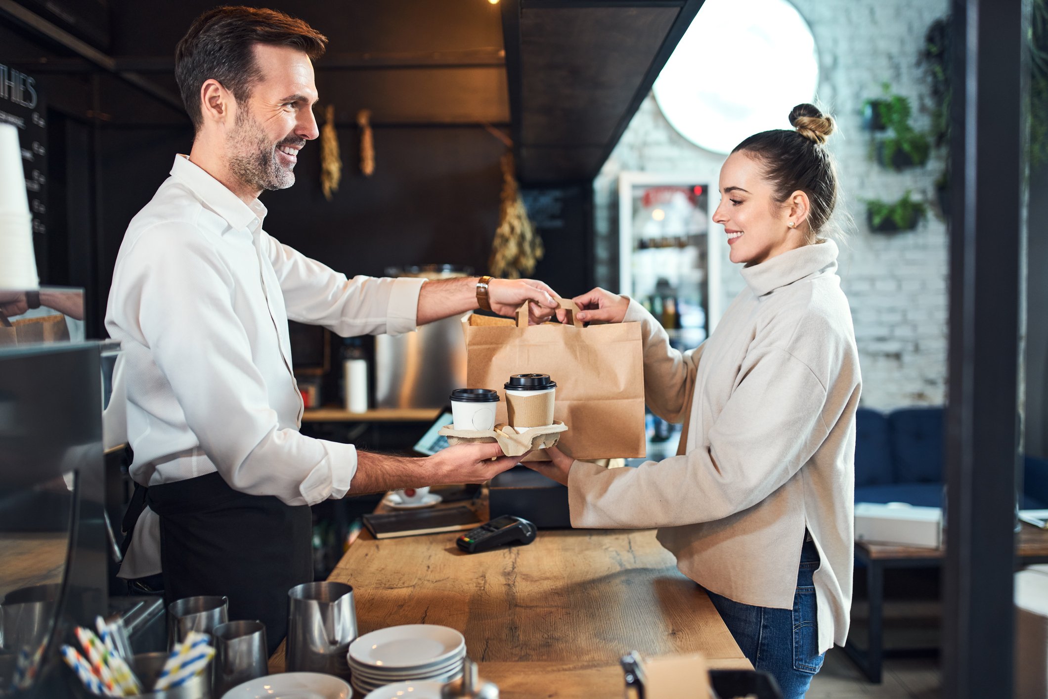 A customer at a coffee shop receiving their order from an  employee.