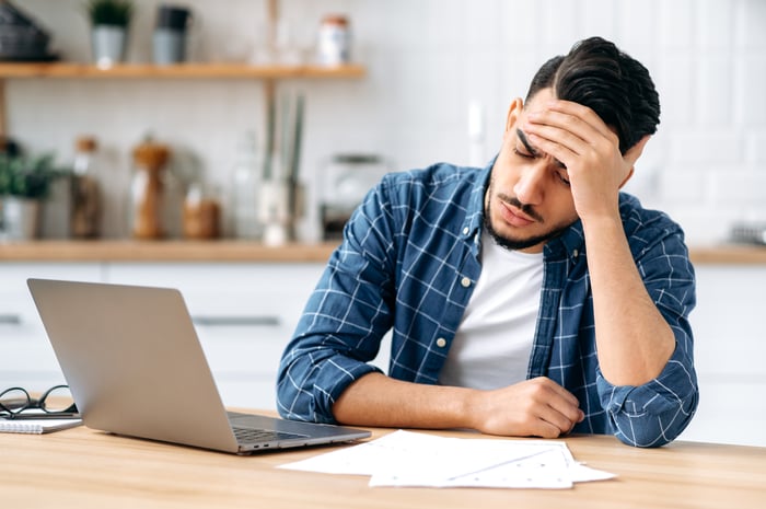 A person at a laptop holding their head.