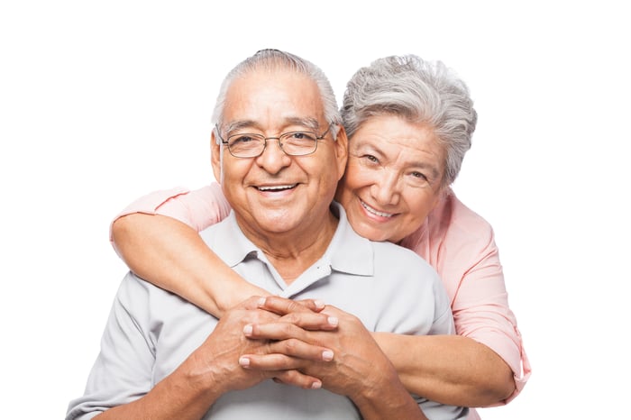 A happy couple is smiling toward the camera, with one embracing the other.