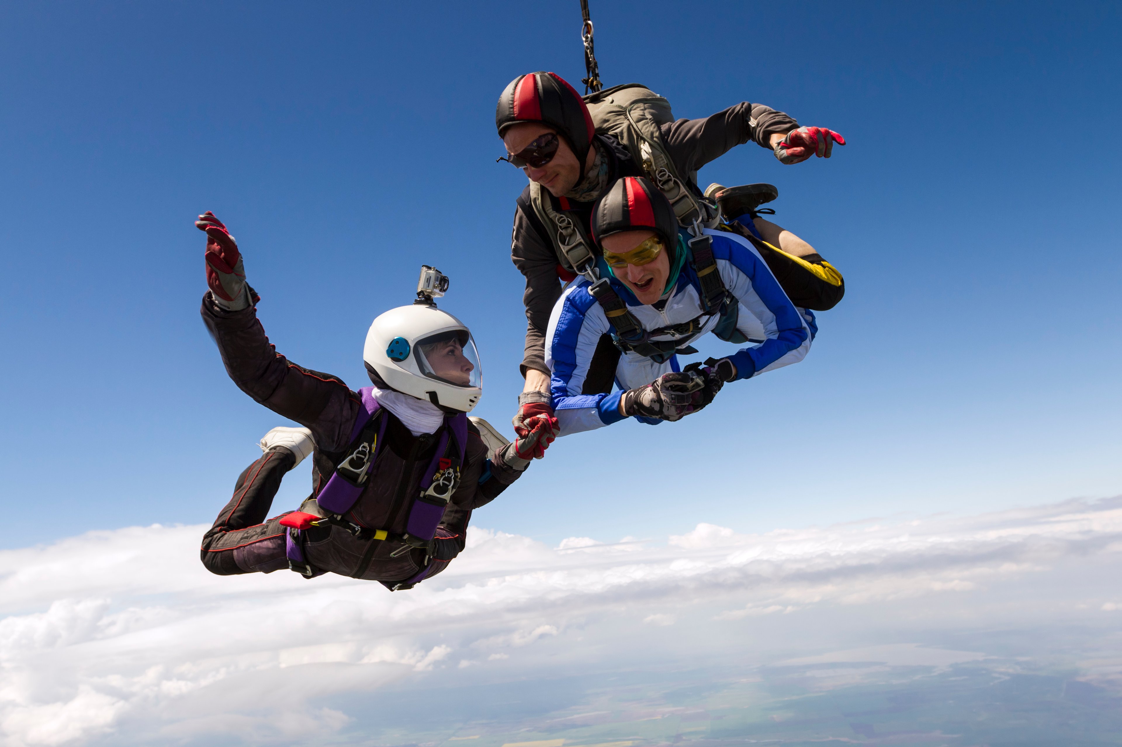 Three smiling people skydiving together.