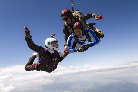 Three smiling people skydiving together.