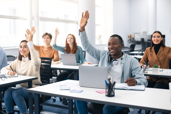 College students raising their hands in a classroom.