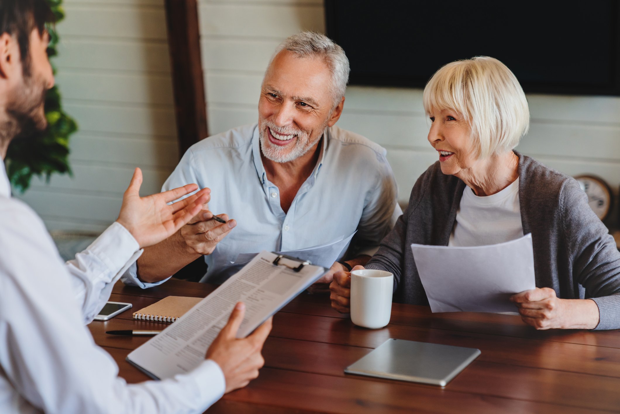 Two people talking with a financial planner while seated at a wooden desk.