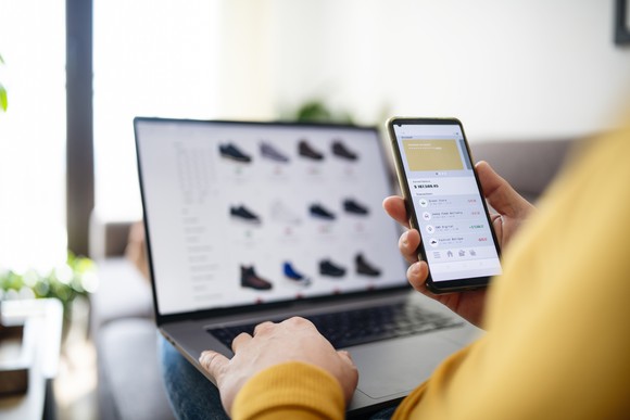 A person looks at their phone while shopping for shoes online.