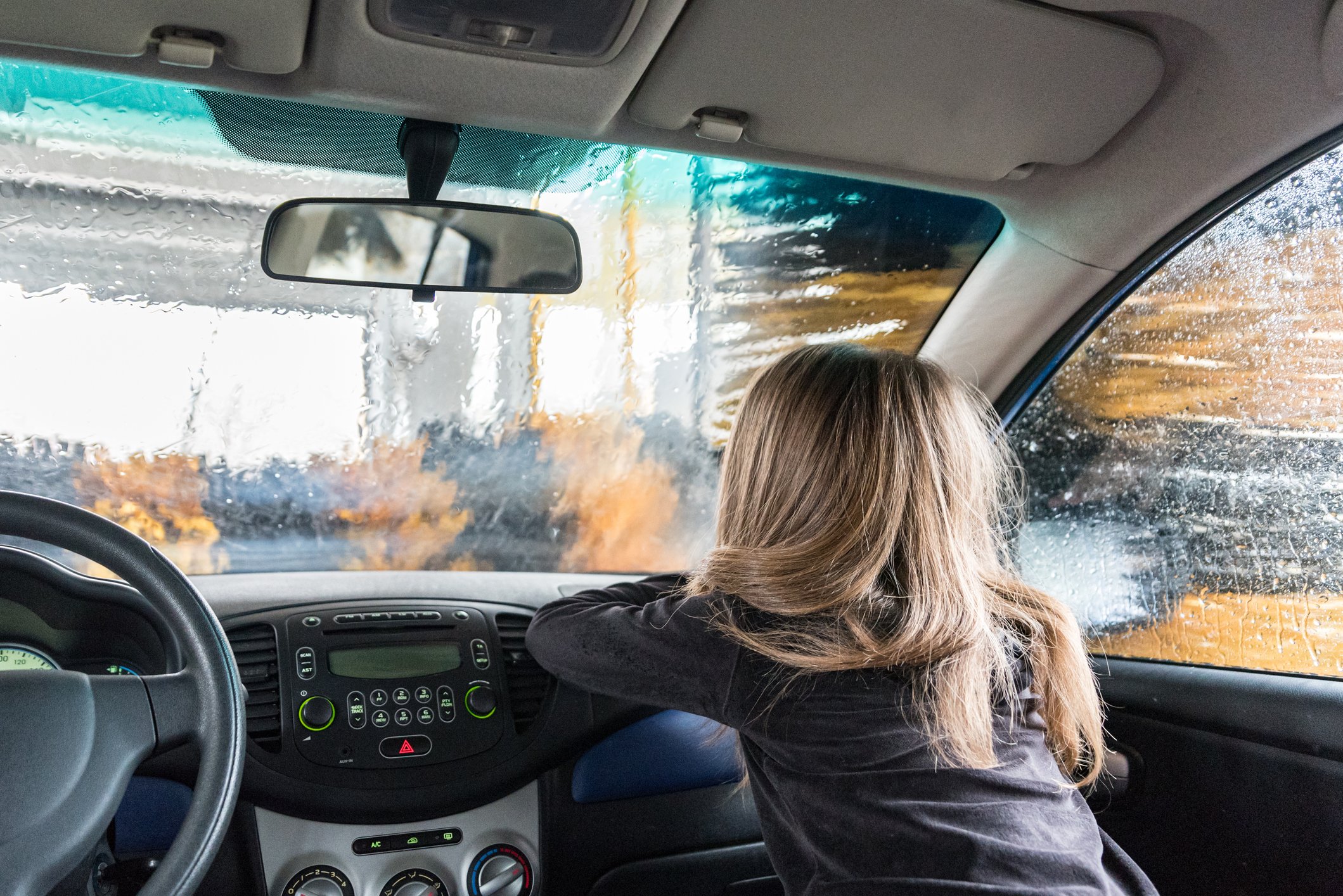 A child looks through the windshield of a car inside a car wash.