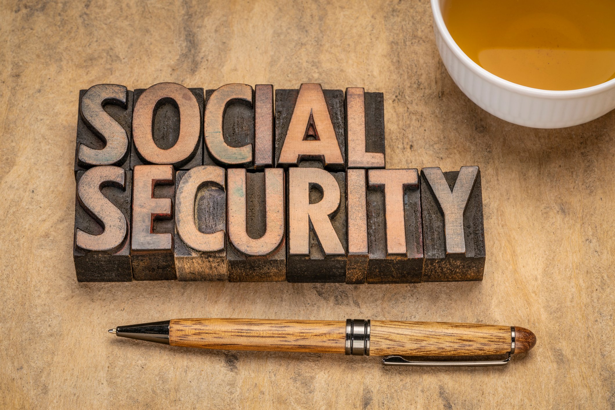 Social Security carved in wood next to a cup of coffee and a pen.
