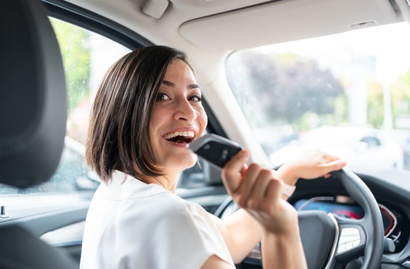 A smiling person in the driver's seat of a new car holds up the keys. 