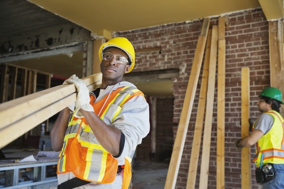A construction worker carrying wood on site.