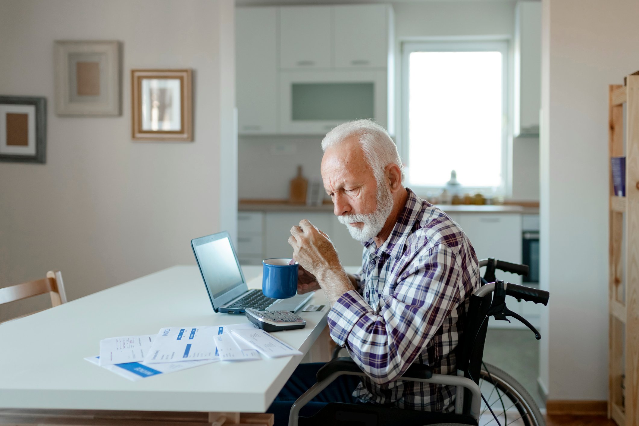 Person in wheelchair sitting at a table with a laptop, calculator, and paper.