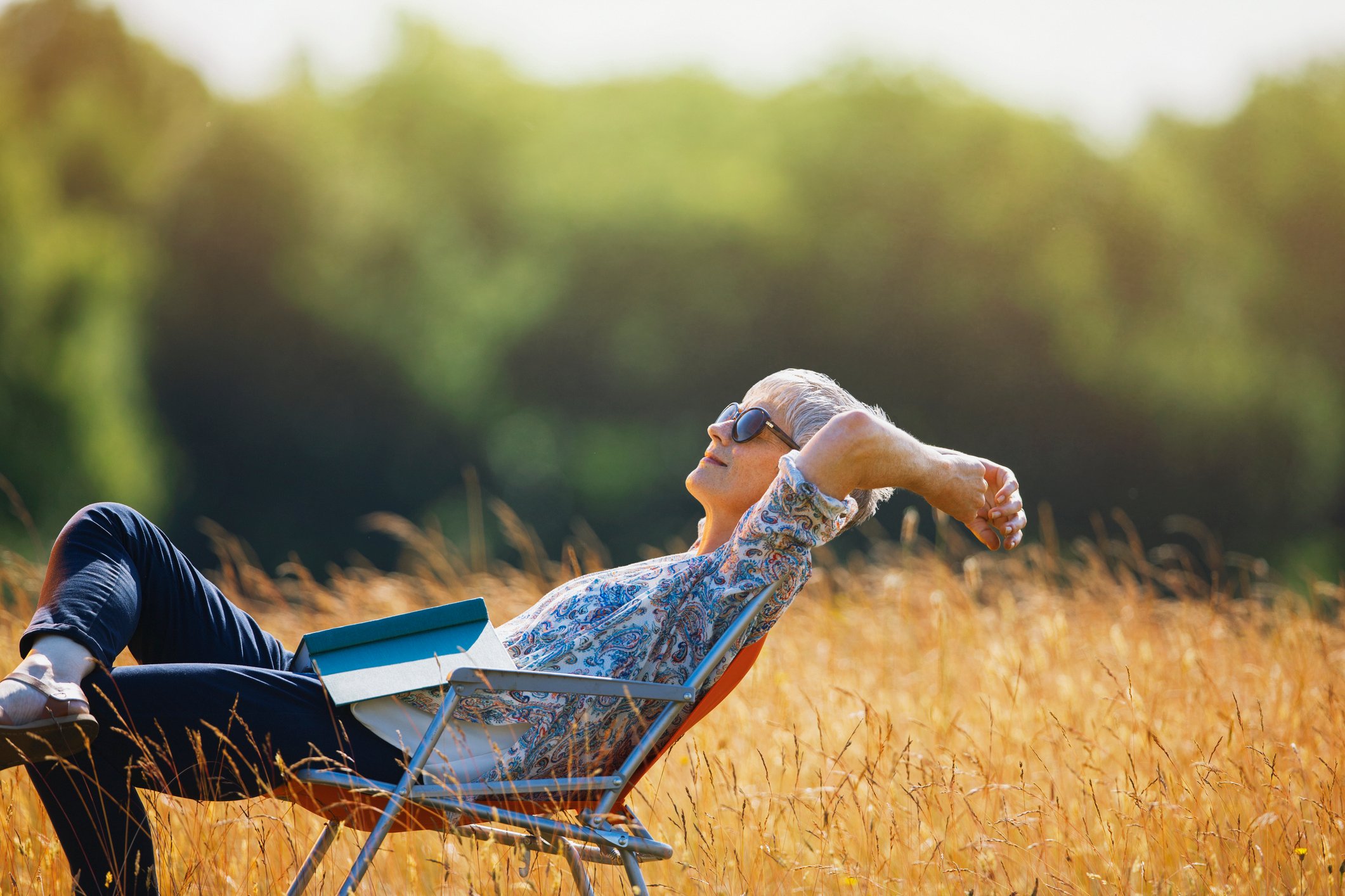 Someone sitting in a lawn chair in the grass with a book opened on their lap.