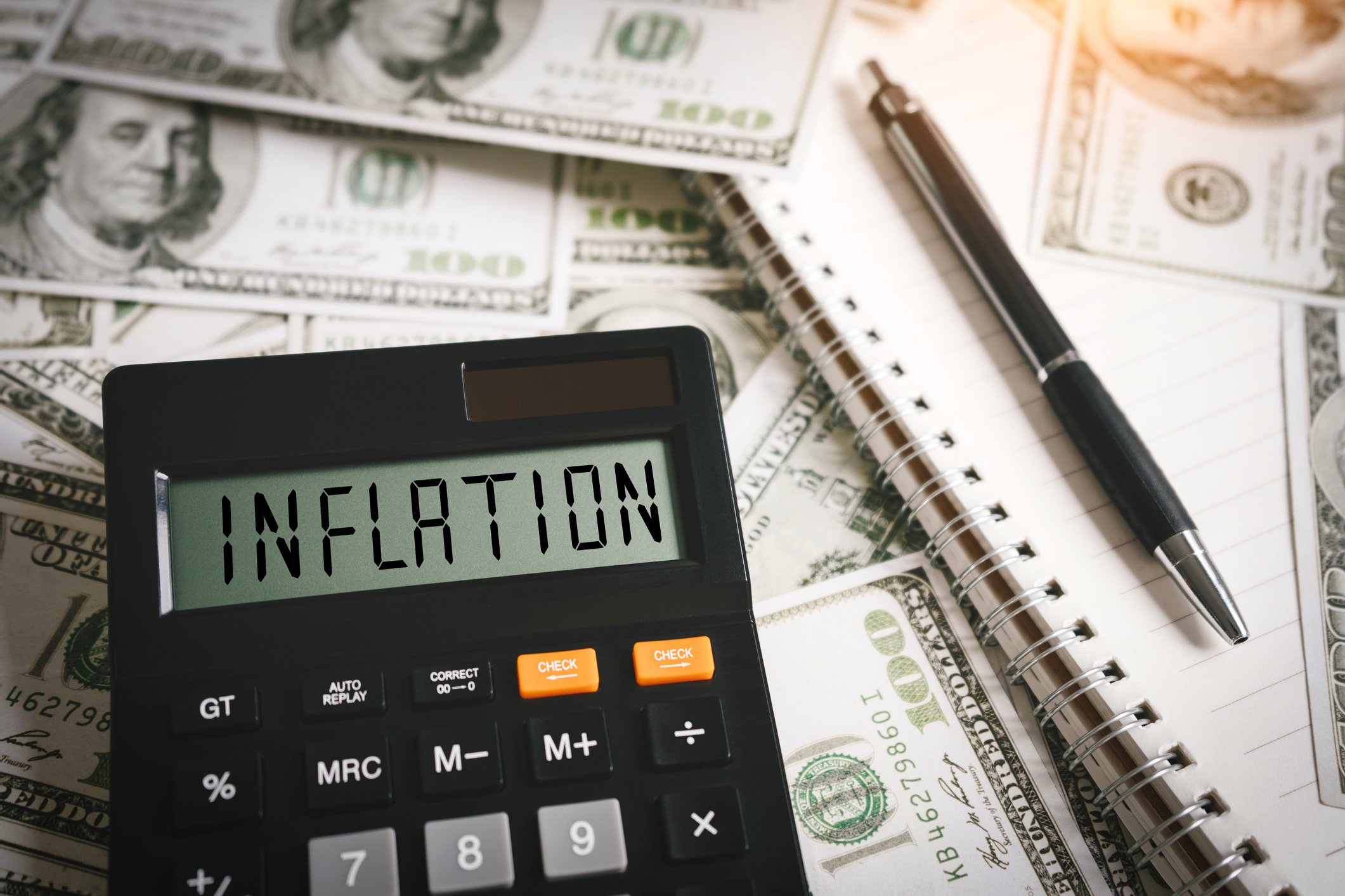 The word inflation typed on a calculator resting on 100 dollar bills.