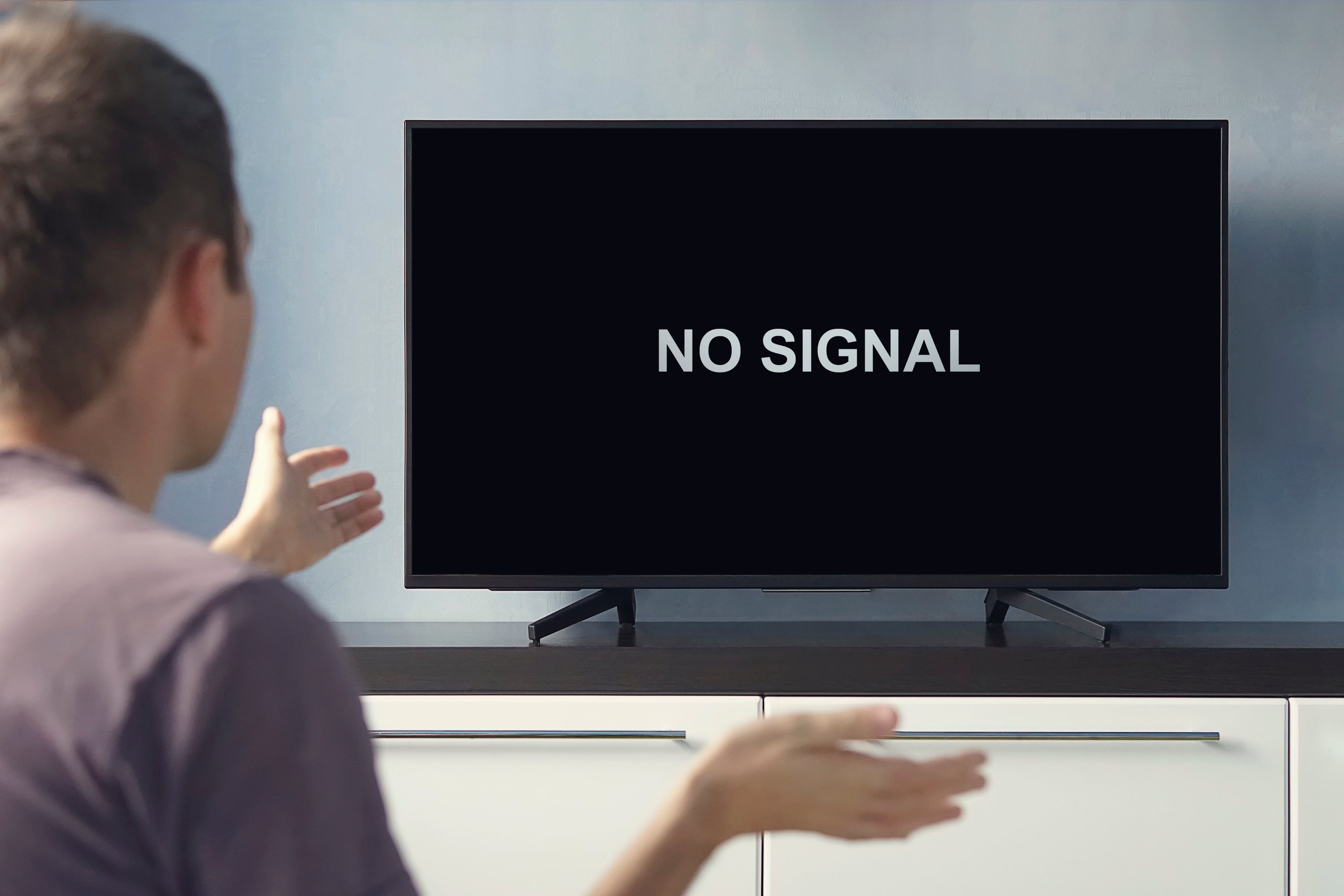 Person staring at black TV screen with white words saying No Signal. 